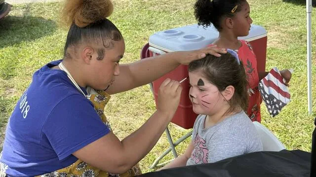 Cherokee West paints Kaushean Coopers face as a cat at the Garland festivities Saturday.
                                 Trevon McGlone | Sampson Independent